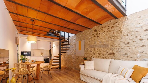 Ein gemütliches Wohnzimmer mit Steinwand, einem weißen Sofa und einem Holzespeisetisch mit Stühlen.