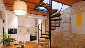 Eine moderne Küche mit weißen Schränken, einem eingebauten Ofen und einem Holzespeisebereich mit Stühlen. Eine Wendeltreppe führt auf eine obere Ebene.