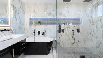 Un baño moderno con una bañera independiente, ducha con mampara de vidrio y un espejo grande.