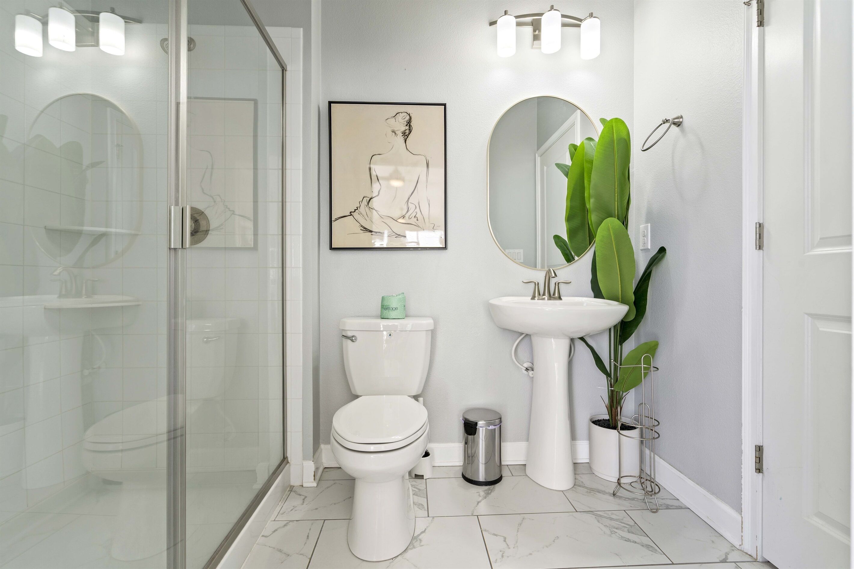 A modern bathroom with a glass shower enclosure, a toilet, a sink, and a large mirror.