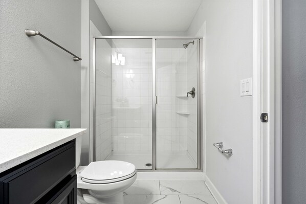 A modern bathroom with a toilet, a shower with a glass door, and a white countertop.