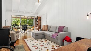A modern living room with a sectional sofa, a fireplace, a dining area, and a large window offering a view of greenery. - Senang in Blackheath (Blackheath)