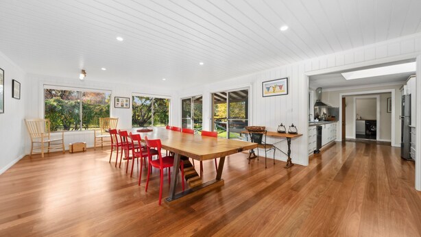 A spacious kitchen with wooden flooring, a large dining table with red chairs, and a view of the outdoors through large windows. - Senang in Blackheath (Blackheath)