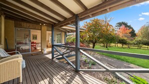 A wooden deck with outdoor furniture, a covered patio area, and a view of a landscaped garden with trees. - Senang in Blackheath (Blackheath)
