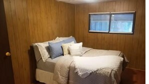 Un dormitorio con cama, paredes de madera y una ventana.