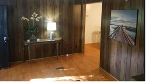 Una habitación con paredes de paneles de madera, suelo de madera, un escritorio con una lámpara, un cuadro y una puerta.