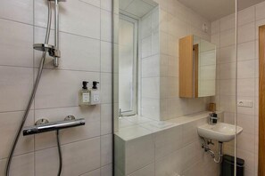 A modern bathroom with a shower, a sink, and a mirror. - Thomsen Residence Suites (Reykjavik)