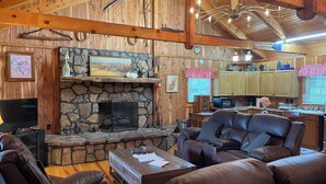 A cozy living room with a stone fireplace, leather sofas, wooden beams, and a kitchen area with wooden cabinets. - Cozy 2bedroom mountain cabin on 18 acres near the Appalachian Trail (Chilhowie)