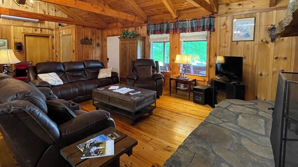 A cozy log cabin interior with leather sofas, a stone fireplace, wooden walls, and a chandelier. - Cozy 2bedroom mountain cabin on 18 acres near the Appalachian Trail (Chilhowie)