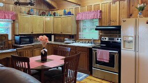 A rustic kitchen with wooden cabinets, a stainless steel refrigerator, a microwave, and a stove. - Cozy 2bedroom mountain cabin on 18 acres near the Appalachian Trail (Chilhowie)