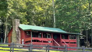 A red wooden cabin with a green roof, surrounded by a wooden fence and lush green trees. - Cozy 2bedroom mountain cabin on 18 acres near the Appalachian Trail (Chilhowie)