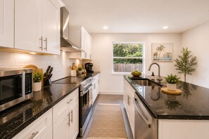 Una cocina moderna con electrodomésticos de acero inoxidable, armarios blancos y un amplio ventanal con vistas a zonas verdes.