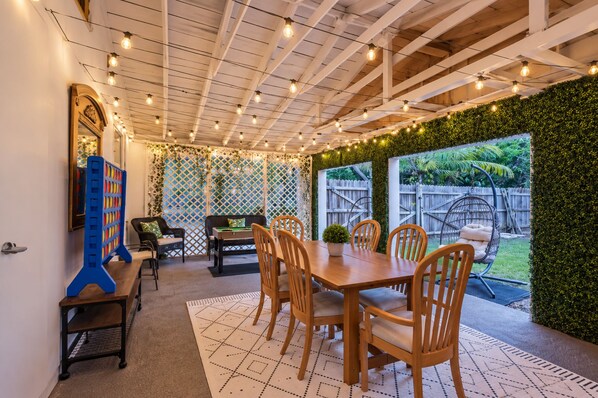 Un patio al aire libre con una mesa y sillas de madera, mesa de billar y una silla colgante.