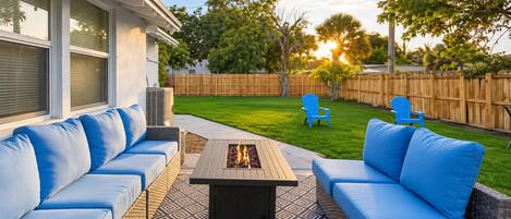 Une terrasse extérieure avec un foyer, deux canapés bleus et deux fauteuils bleus.
