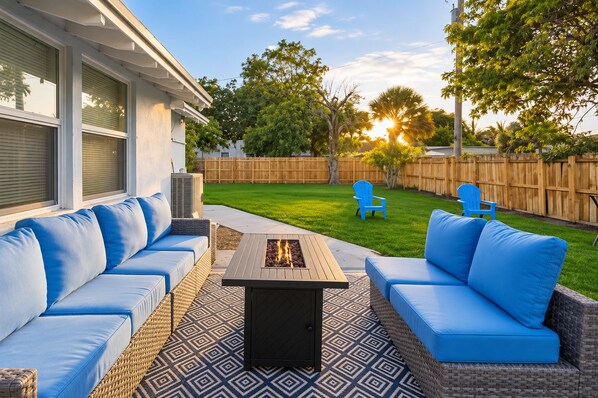 Une terrasse extérieure avec un foyer, deux canapés bleus et deux fauteuils bleus.
