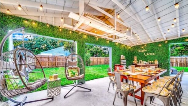An outdoor dining area with a green wall, hanging chairs, and a table set for a meal. - 6Bed Near Beach - Grill, Pool Table, FirePit - Family & Event Open (West Palm Beach)