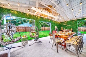 Ein Essbereich im Freien mit grüner Wand, Hängesesseln und einem für eine Mahlzeit gedecktem Tisch.