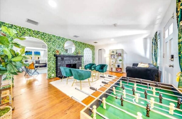 Ein Wohnzimmer mit Kicker, grünen Sesseln, einem Kamin und einem Bücherregal.
