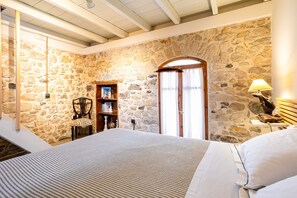 Una camera da letto con pareti in pietra, un letto di legno, una sedia, una libreria e una lampada.