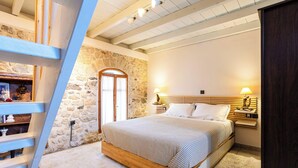 Un dormitori amb paret de pedra, estructura de llit de fusta, tauletes de nit i una escala de fusta.