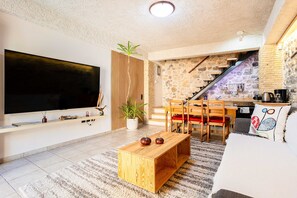 Un salon Ă©quipĂ© dâun tĂ©lĂ©viseur, dâune table basse en bois, dâun canapĂ© et dâun escalier menant Ă la cuisine.