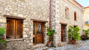 Un edifici de pedra amb persianes de fusta, plantes en testos i un carrer empedrat.