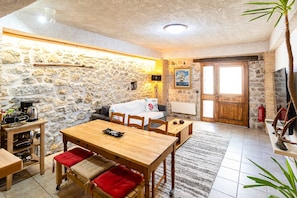 A cozy room with a stone wall, wooden furniture, a fireplace, and a large window. - Limni Stone Apartments (Mantoudi-Limni-Agia Anna)