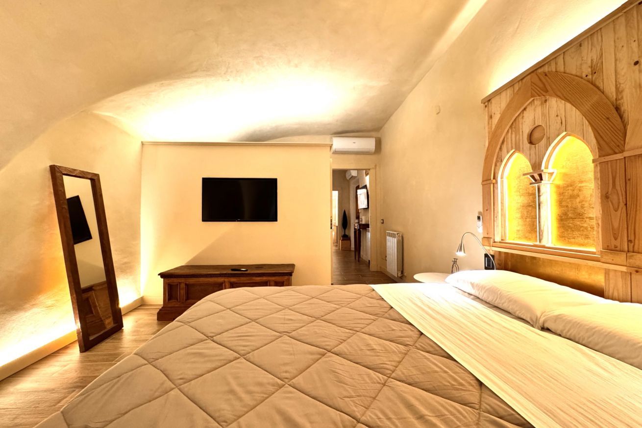 Una camera da letto con un letto grande, una finestra ad arco in legno, una TV a schermo piatto e uno specchio.