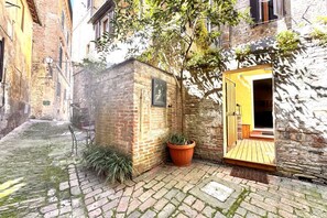 A narrow alley with a small brick building, a potted plant, and a wooden door. - Stalloregis 19 - near the Duomo (Siena)