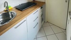 A kitchen with white cabinets, a stainless steel sink, a wooden countertop, and a black tablet.