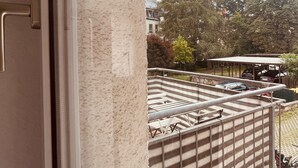A balcony with a metal railing, a view of parked cars, and a building in the background.