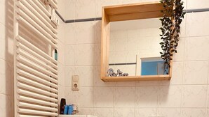 A bathroom with a white sink, a mirror, a towel rack, a heater, and a trash bin.