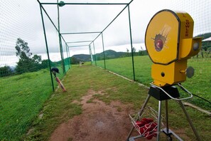 Un filet d’entraînement de cricket, avec une machine à lancer et une batte de cricket appuyée contre.
