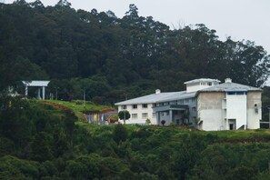 Un grand bâtiment doté d’un toit plat et d’une petite tour, entouré d’une végétation luxuriante et d’arbres.