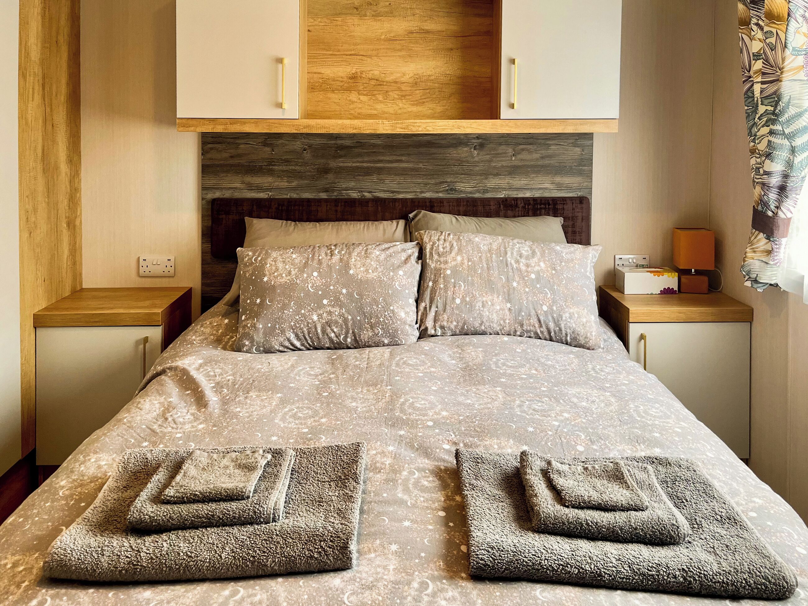 Een net opgemaakt bed met behangpatroon en twee opgevouwen handdoeken.