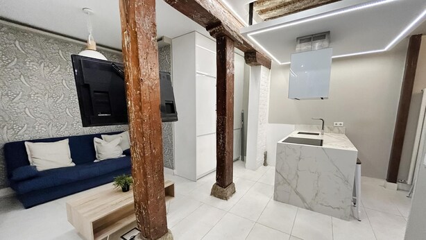 Un salón moderno con sofá azul, vigas de madera, televisor y lavamanos de mármol.