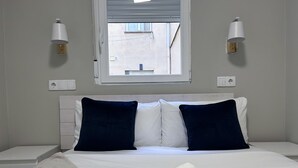 Una habitación de hotel con una cama, dos lámparas de pared, un ventanal y vistas al exterior.
