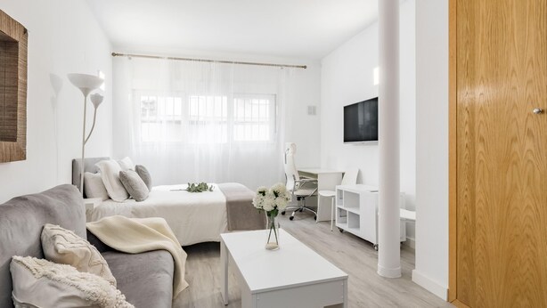 A modern, minimalist living room with a grey sofa, a white coffee table, and a TV mounted on the wall.