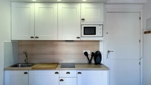 A compact kitchen with white cabinets, a microwave, a sink, and a wooden countertop. - Sol Studio III - Apartment in the City Center with Balcony (Madrid)