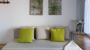 A modern living room with a grey sofa, two green cushions, and a white throw blanket. There are two abstract paintings on the wall and a vase with white flowers on a side table. - Sol Studio III - Apartment in the City Center with Balcony (Madrid)