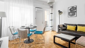 A modern living room with a dining area, featuring a sofa, coffee table, and chairs. - La Latina Life - 2-Bedroom Apartment with Balcony (Madrid)