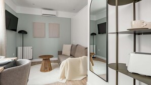 Ett modernt vardagsrum med en soffa, ett soffbord, en fåtölj, en golvlampa, en tv och en bokhylla.