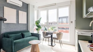 Una sala de estar moderna con un sofá verde, una mesa de centro redonda de madera y un comedor con una mesa pequeña y sillas.