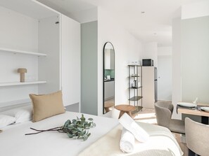 A modern hotel room with a bed, a bedside table, a mirror, a small round table, and a seating area with chairs.
