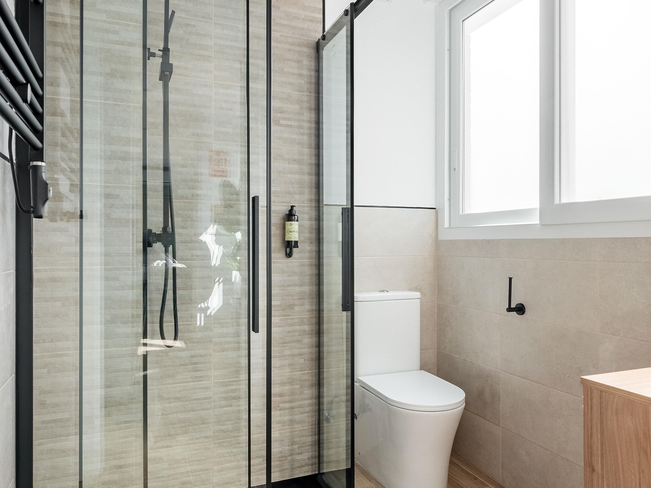 Un baño moderno con cabina de ducha de vidrio, inodoro blanco y mueble de madera.