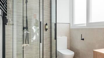 Un baño moderno con cabina de ducha de vidrio, inodoro blanco y mueble de madera.