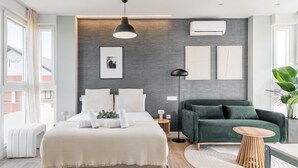 A modern bedroom with a bed, bedside tables, a green sofa, a round wooden table, and a large window.