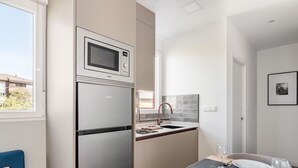Eine kleine Küche mit integriertem Mikrowellenherd, einem Kühlschrank und einem Spülbecken mit modernem Wasserhahn.
