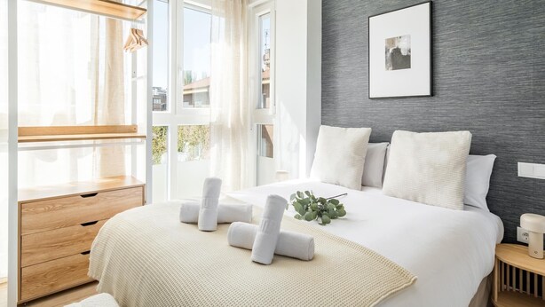 Ein modernes Schlafzimmer mit einem großen Bett, einem Holznachttisch, einem Schreibtisch und einem Fenster mit Vorhängen.