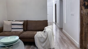 A modern living room with a brown sofa, striped pillows, a glass coffee table, and a white throw blanket. - Madrid Experience - 3-Bedroom Apartment in the City Center (Madrid)